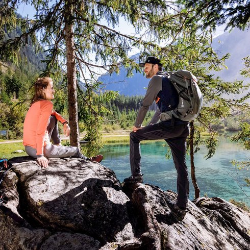 Smaragdhotel Tauernblick – Ihr 4-Sterne-Hotel am Wildkogel Zwei Wanderer ruhen auf Felsen an einem Bergsee mit Wald und Bergen