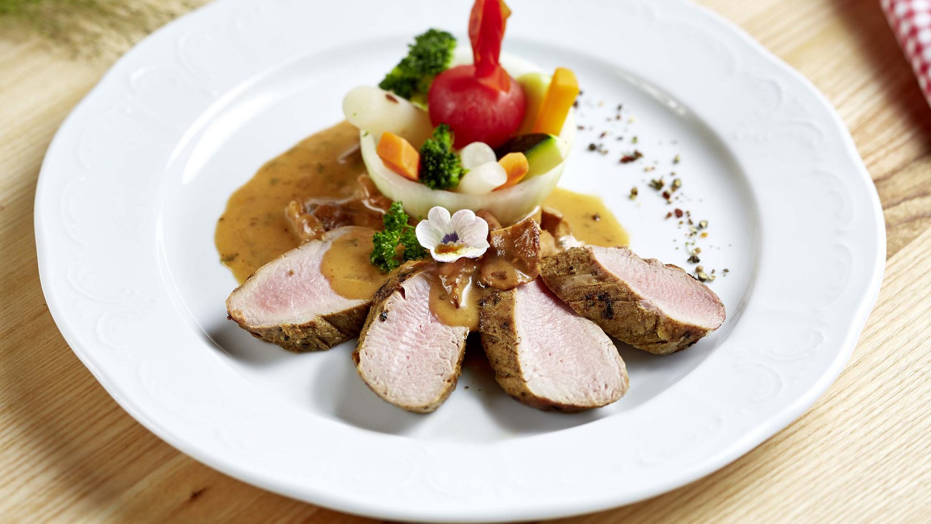 Wellnesshotel Salzburgerland: Smaragdhotel Tauernblick Gebackene Fleischscheiben mit Soße und bunt dekoriertem Gemüse auf weißem Teller