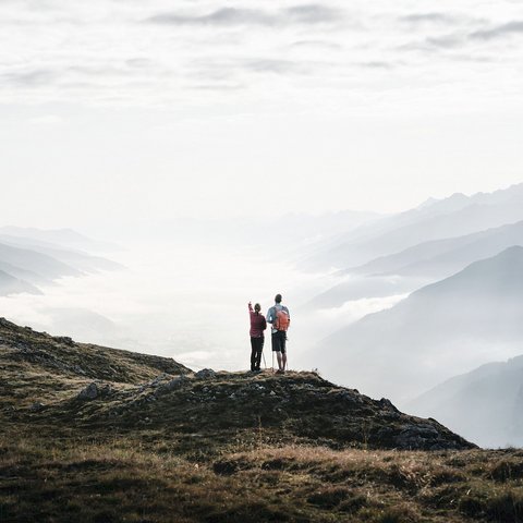 Erlebnisse.jpg Zwei Wanderer stehen auf einem Bergkamm mit Blick auf wolkenbedeckte Berge