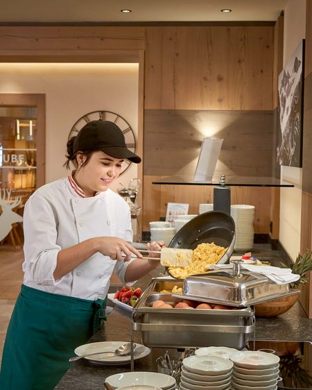 Salzburgerland: wellness hotel with 4 stars and cuisine Chef serving scrambled eggs into buffet container in a restaurant