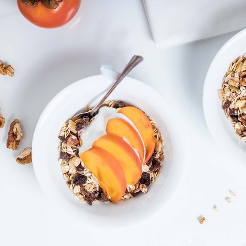 Die besten Hotels im Salzburgerland Schalen mit Müsli, Joghurt, Walnüssen und Persimonenscheiben auf weißem Tisch