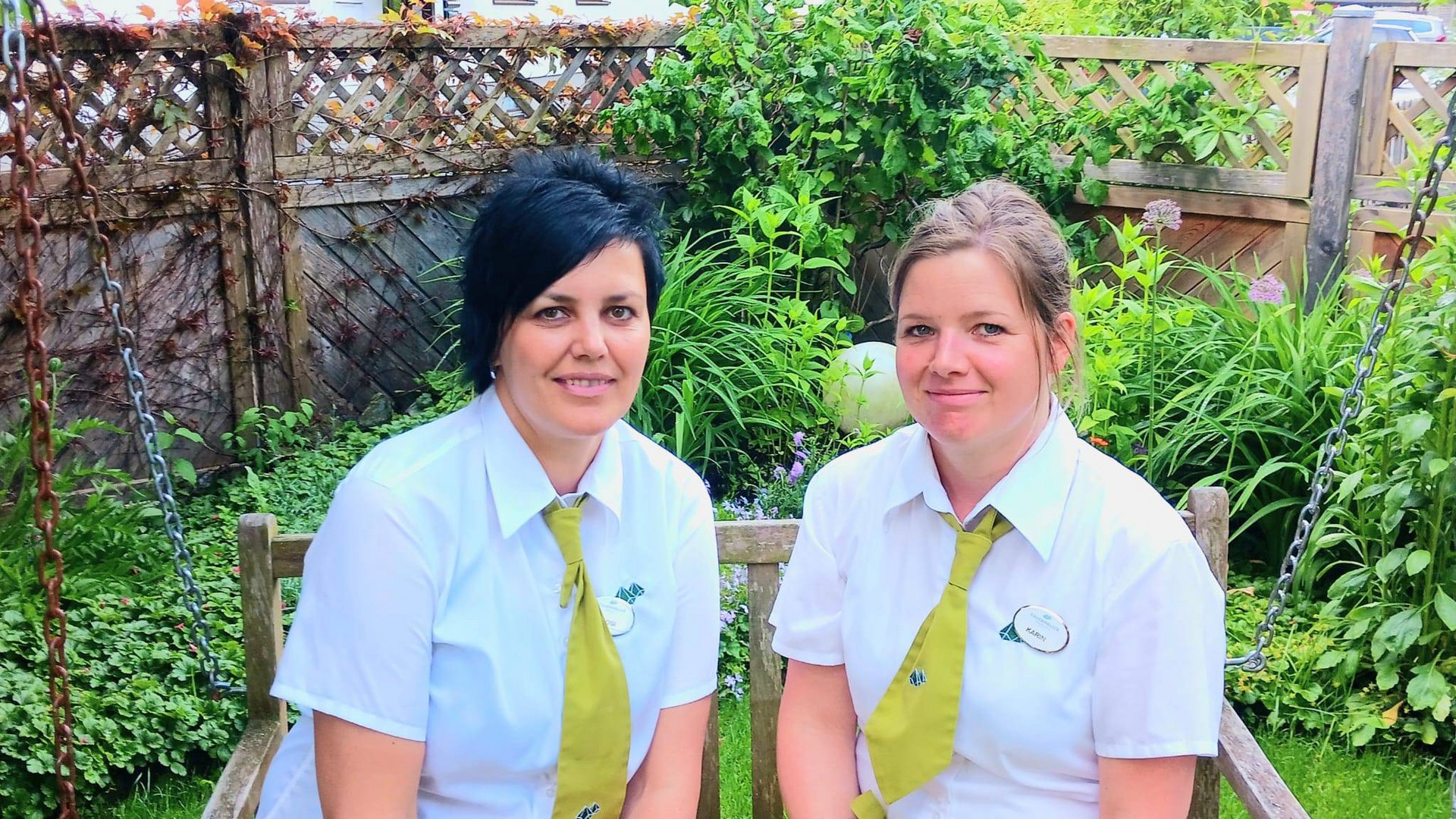 Wildkogel: Hotel mit Blick für das Besondere Zwei Frauen in weißen Hemden und grünen Krawatten sitzen auf einer Gartenschaukel