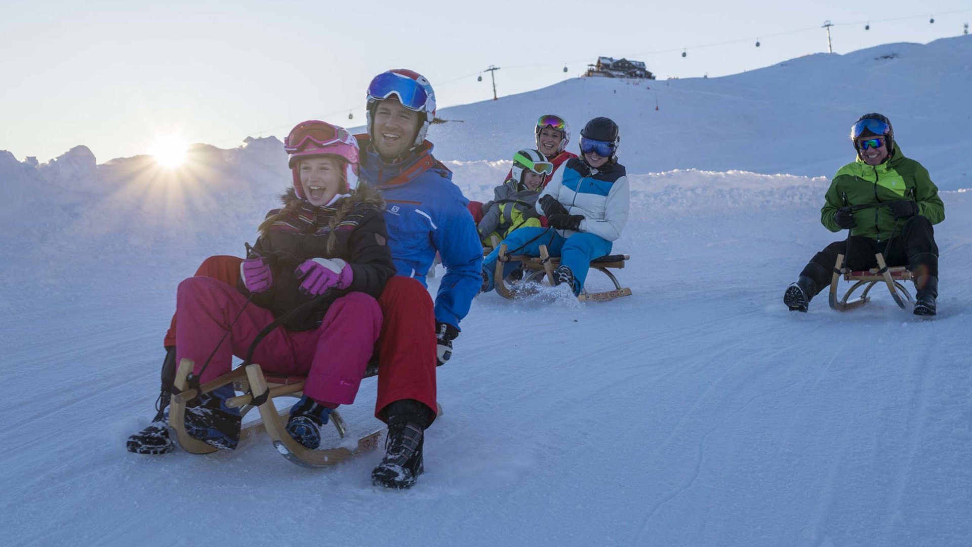 Spaß beim Rodeln: Bramberg am Wildkogel Mehrere Personen rodeln fröhlich bei Sonnenuntergang auf einer verschneiten Piste
