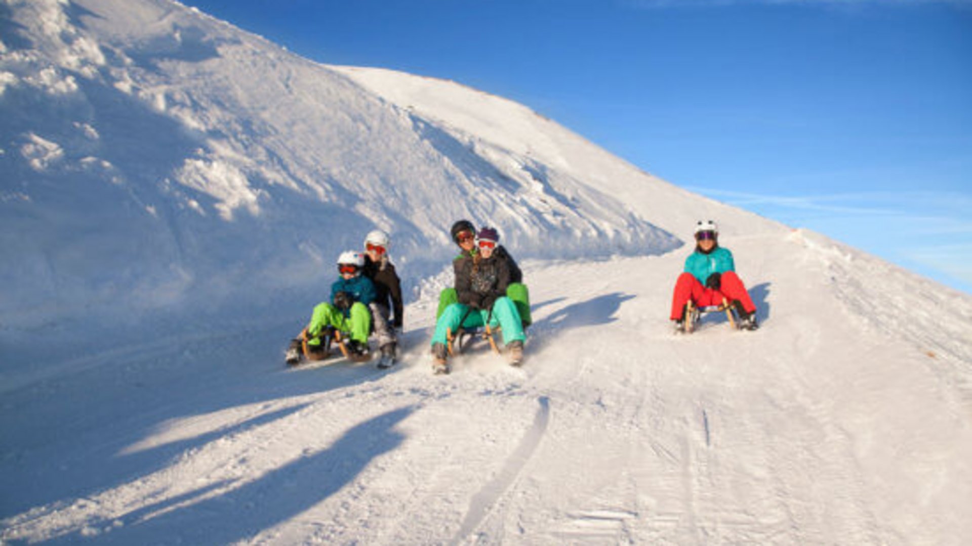 Skiing holidays in Salzburgerland: Smaragdhotel Tauernblick Family members sledding down a snowy hill under clear blue sky