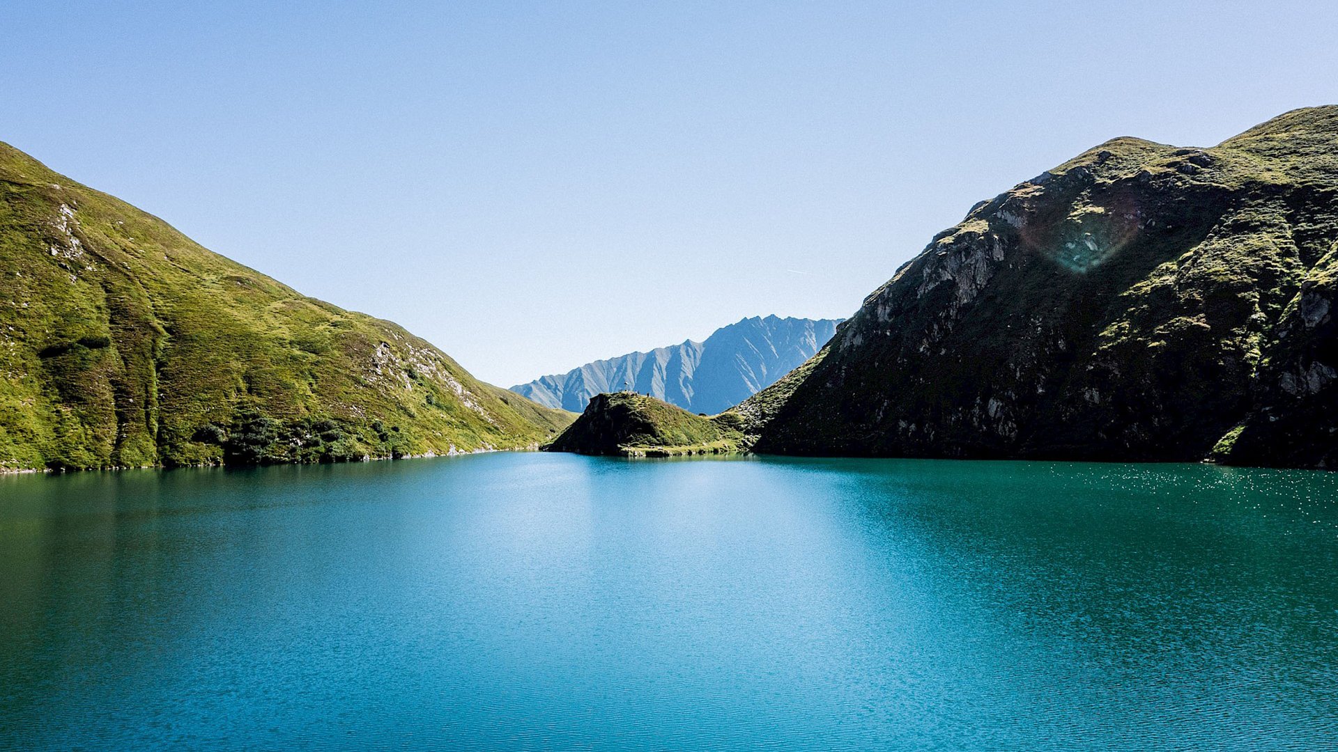 Familienhotel: Österreich im Sommer erleben Bergsee mit klar blauem Wasser und grünen Hügeln unter klarem Himmel