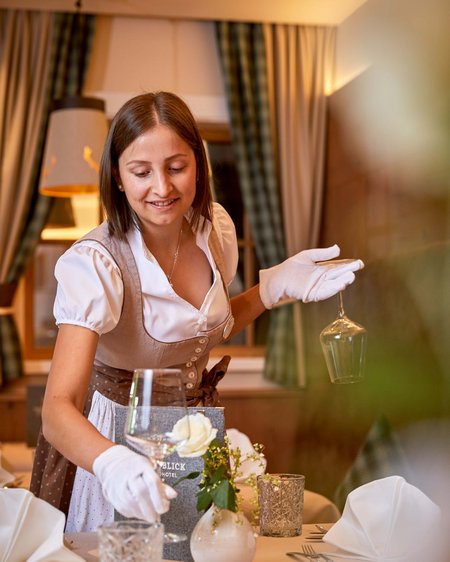 Wanderurlaub in Österreich und mehr Kellnerin im Dirndl deckt elegant einen Tisch mit Gläsern und Blumen