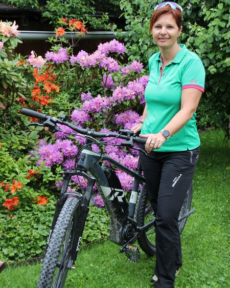 Hohe Tauern National Park: holiday for bikers Woman in green polo posing with mountain bike in front of blooming bushes