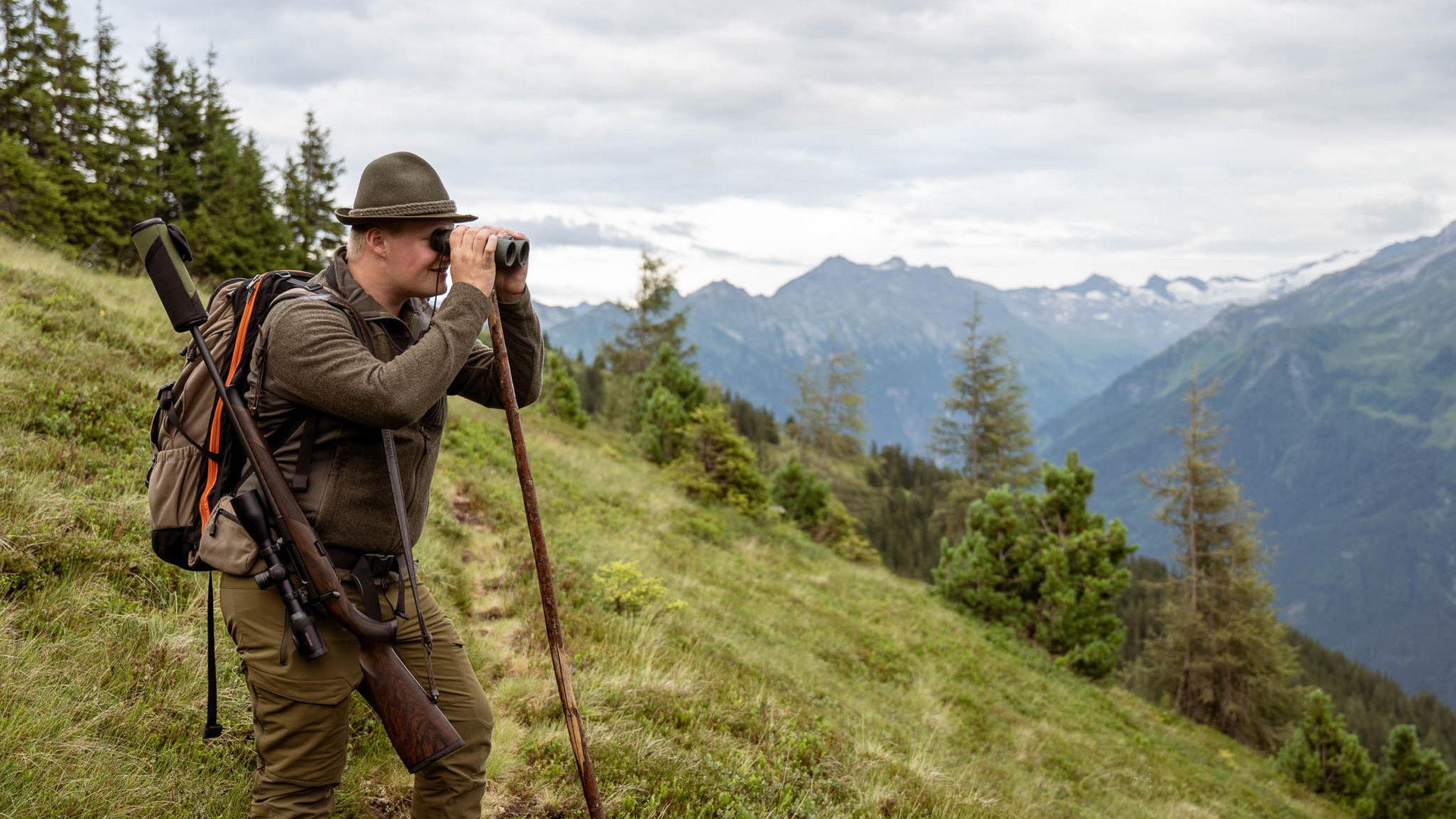 Mit Christoph ins Revier: Wildbeobachtung zwischen 1.600 und 2.000 Metern im Nationalpark Hohe Tauern. Hirsch, Gams, Murmeltiere und im Herbst die Hirschbrunft. Wanderer mit Fernglas und Gewehr vor einer alpinen Berglandschaft