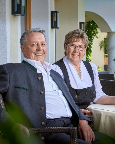 Wildkogel: Hotel mit Blick für das Besondere Älteres Paar in traditioneller Kleidung sitzt draußen an einem Tisch mit Blume