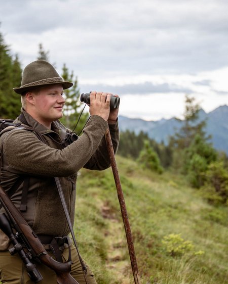 Mit Christoph ins Revier: Wildbeobachtung zwischen 1.600 und 2.000 Metern im Nationalpark Hohe Tauern. Hirsch, Gams, Murmeltiere und im Herbst die Hirschbrunft. Mann mit Hut, Rucksack und Fernglas vor einer Berglandschaft