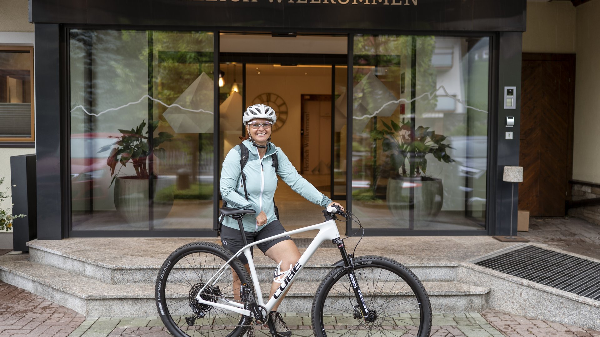 Nationalpark Hohe Tauern: Urlaub für Biker Frau mit Fahrrad steht vor Eingang mit Schild Herzlich Willkommen.