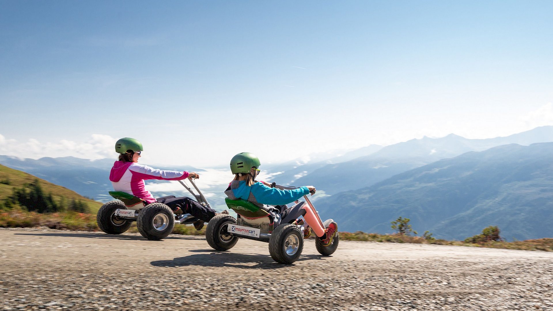 Familienhotel: Österreich im Sommer erleben Zwei Personen fahren Mountaincarts auf einem Bergweg mit Panoramablick
