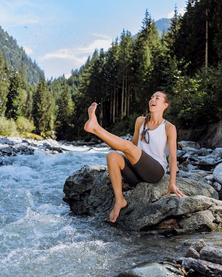 Hotel in Bramberg: Smaragdhotel Tauernblick Woman sitting on rock by river splashing water with foot in forest