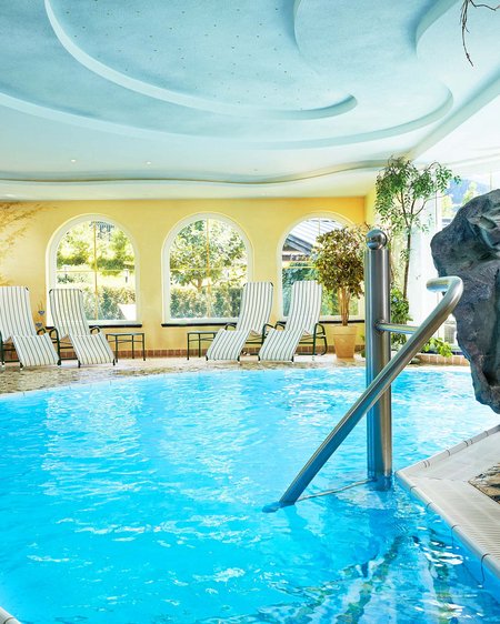 Ihr Pärchenurlaub in Österreich Innenpool mit Liegestühlen und künstlichem Felsen in sonnigem Wellnessbereich