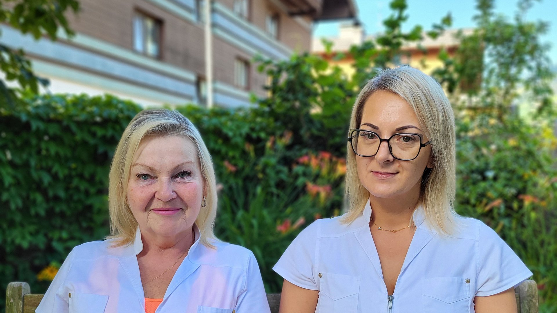 Wildkogel: Hotel mit Blick für das Besondere Zwei Frauen in weißen Arbeitsjacken sitzen auf einer Holzbänk im Garten