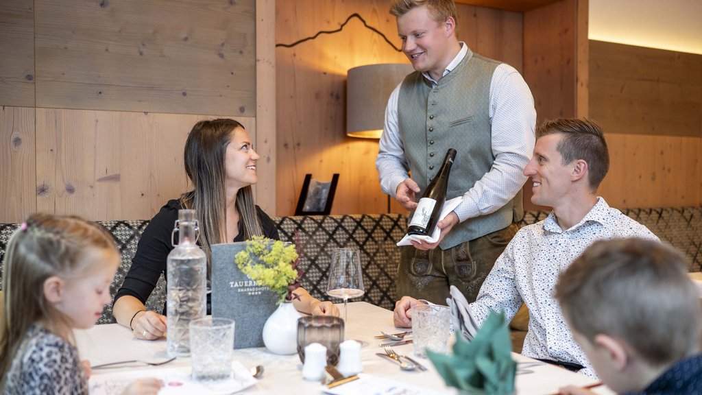 Familienhotel im Salzburger Land: Smaragdhotel Tauernblick Kellner serviert Wein an Tisch mit lächelnden Gästen im Restaurant