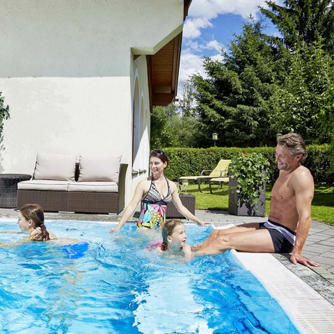 Family hotel in Bramberg: Smaragdhotel Tauernblick Family with two children enjoying the pool in the garden on a sunny day