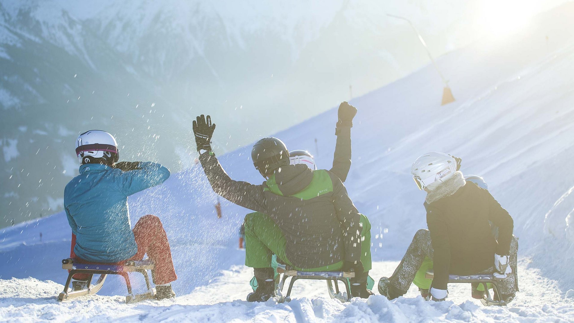 Spaß beim Rodeln: Bramberg am Wildkogel Vier Personen rodeln mit Helmen auf verschneiter Piste im Sonnenschein