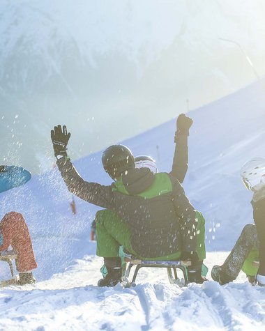 4 Sterne Hotel in Salzburgerland: Smaragdhotel Tauernblick Vier Personen rodeln mit Helmen auf verschneiter Piste im Sonnenschein