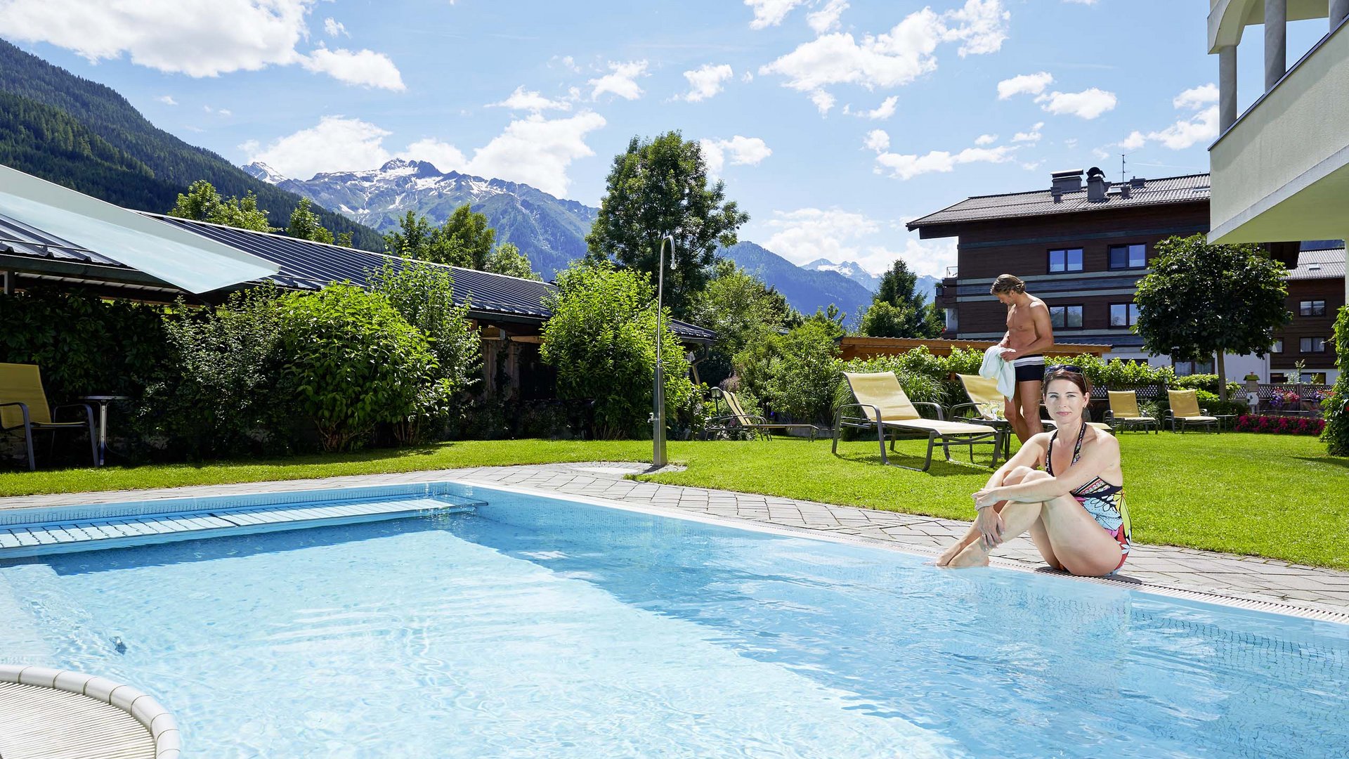 Family hotel in Austria with pool Woman sitting by pool edge with mountain view and sunny weather