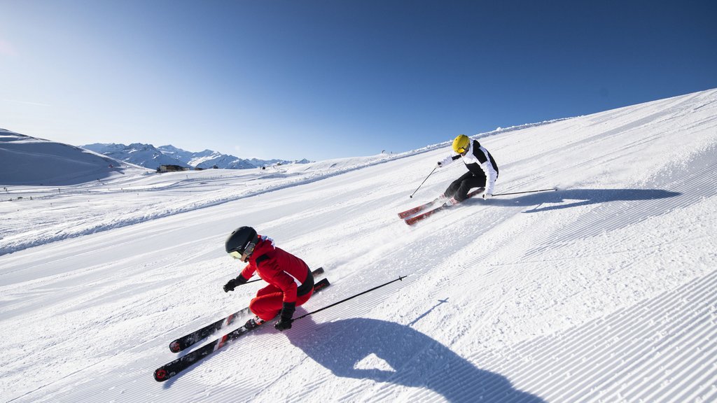 Skiing holidays in Salzburgerland: Smaragdhotel Tauernblick Two skiers skiing down a sunny slope with mountains in the background