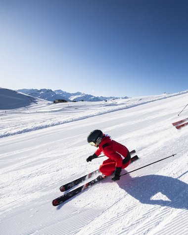 4 Sterne Hotel in Salzburgerland: Smaragdhotel Tauernblick Zwei Skifahrer fahren auf einer sonnigen Skipiste mit Bergen im Hintergrund