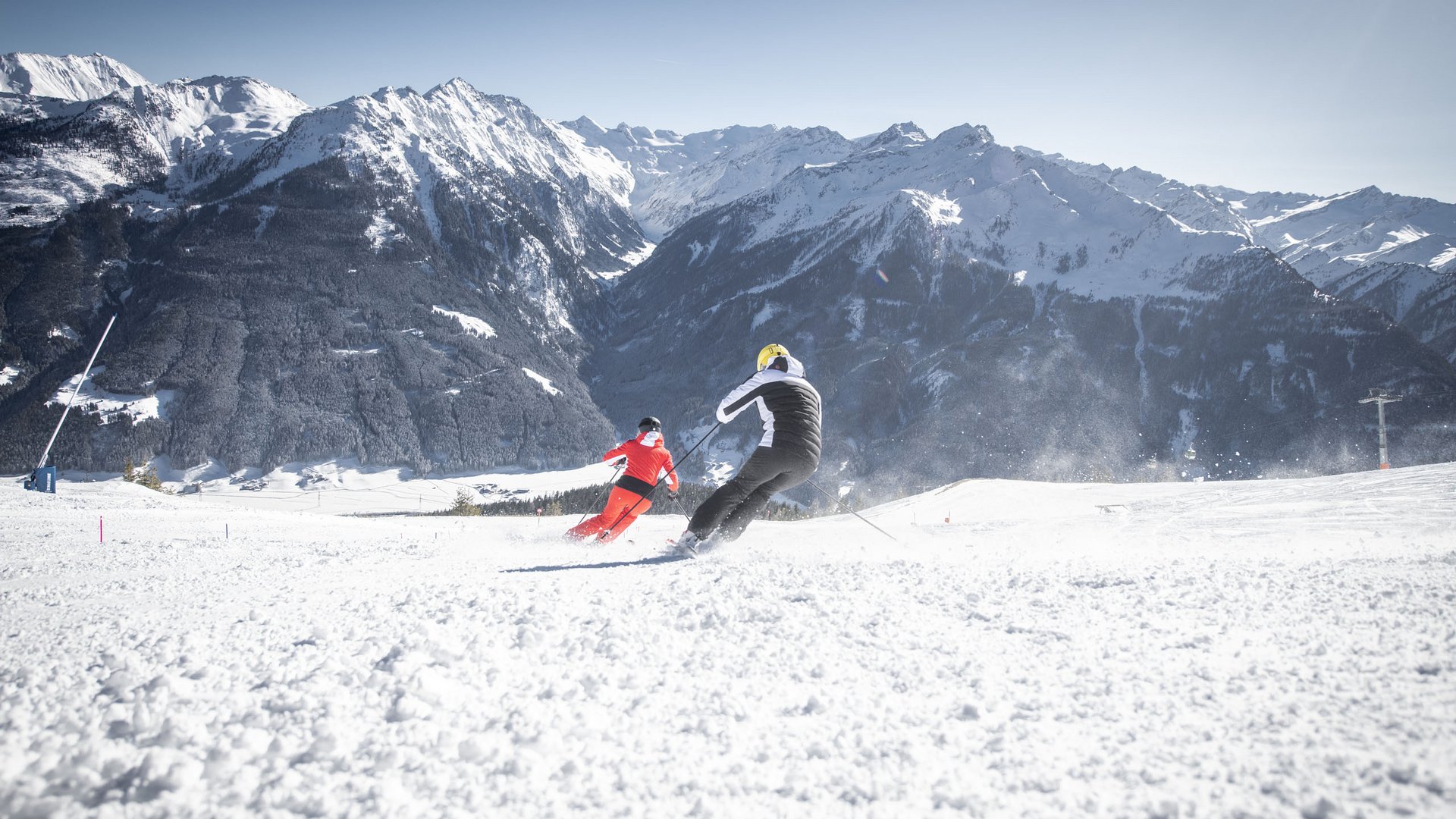 Smaragdhotel Tauernblick – your 4-star hotel near Wildkogel Two skiers skiing on snowy slope with sunny mountain backdrop
