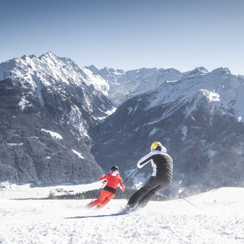 Skifahren Wildkogel Zwei Skifahrer fahren bei Sonnenschein auf verschneiter Piste mit Bergkulisse