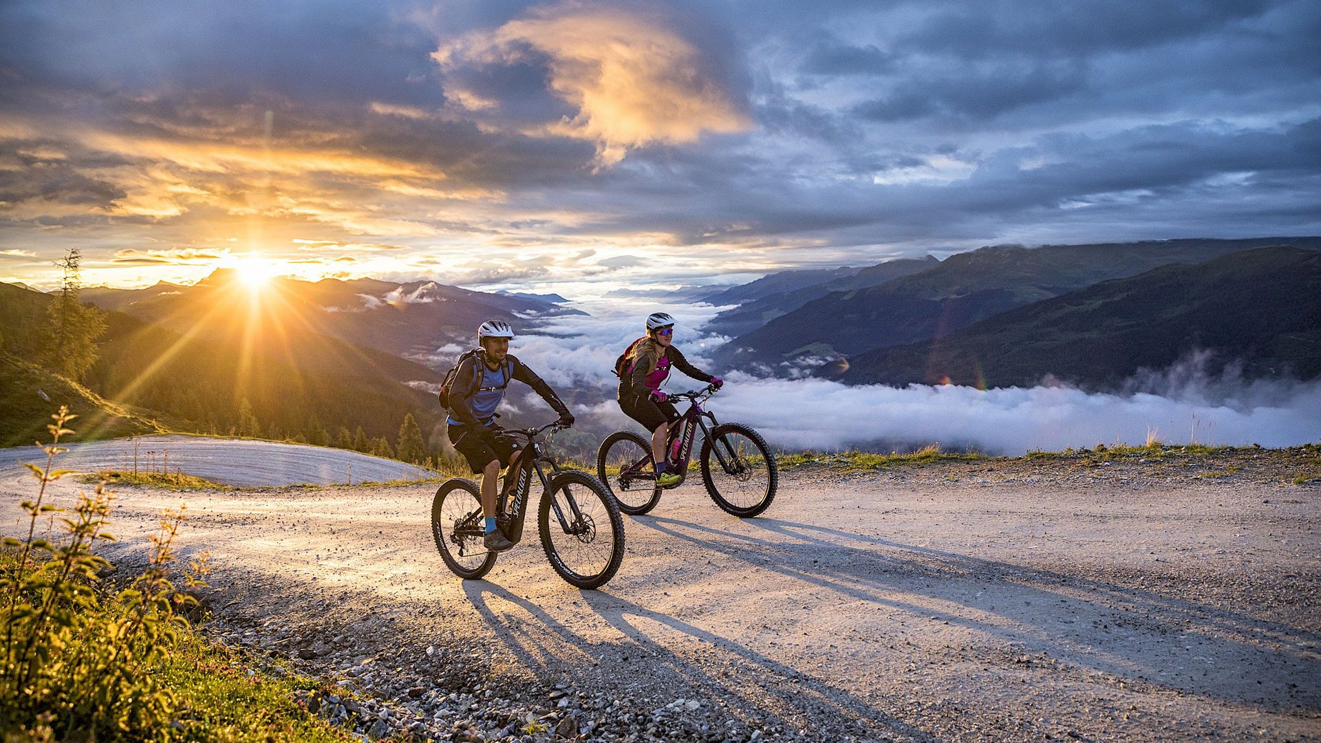 Hohe Tauern National Park: holiday for bikers Two cyclists riding on mountain trail at sunset with fog in valley below