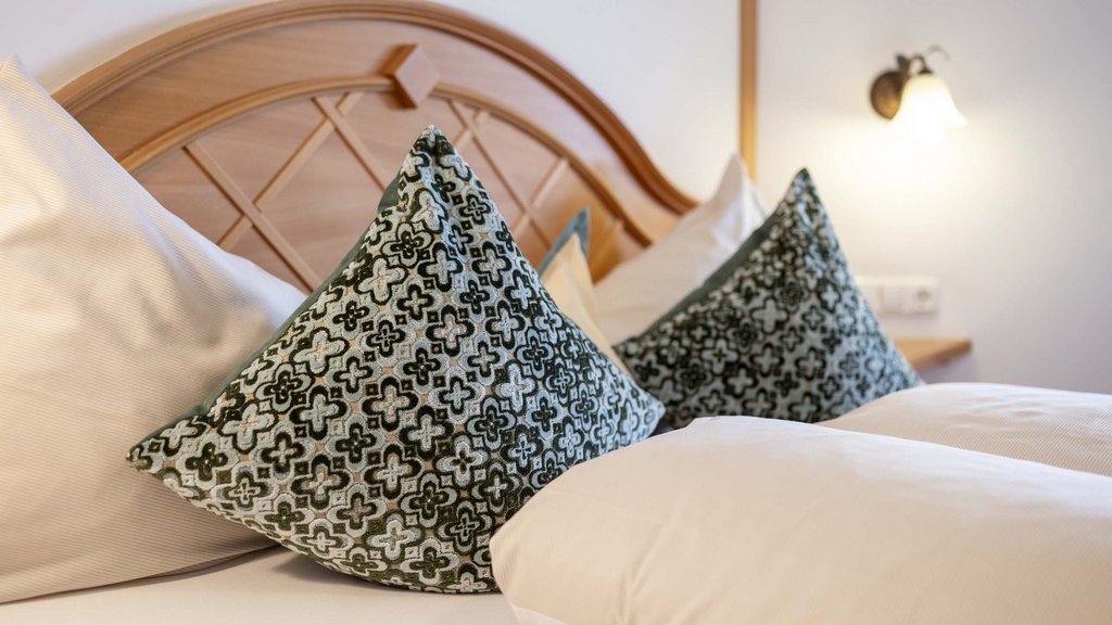 Bramberg am Wildkogel: accommodation Patterned pillows on a bed with wooden headboard and wall lamp in background