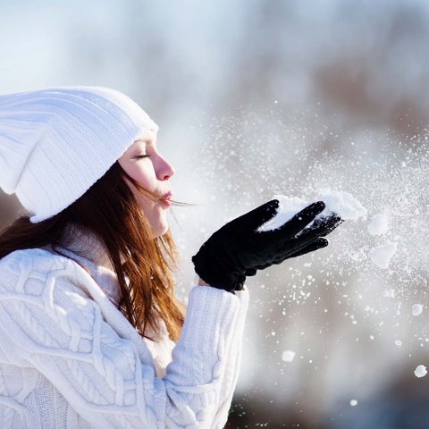 Die besten Hotels im Salzburgerland Frau mit weißer Mütze und Pullover bläst Schnee von schwarz behandschuhter Hand