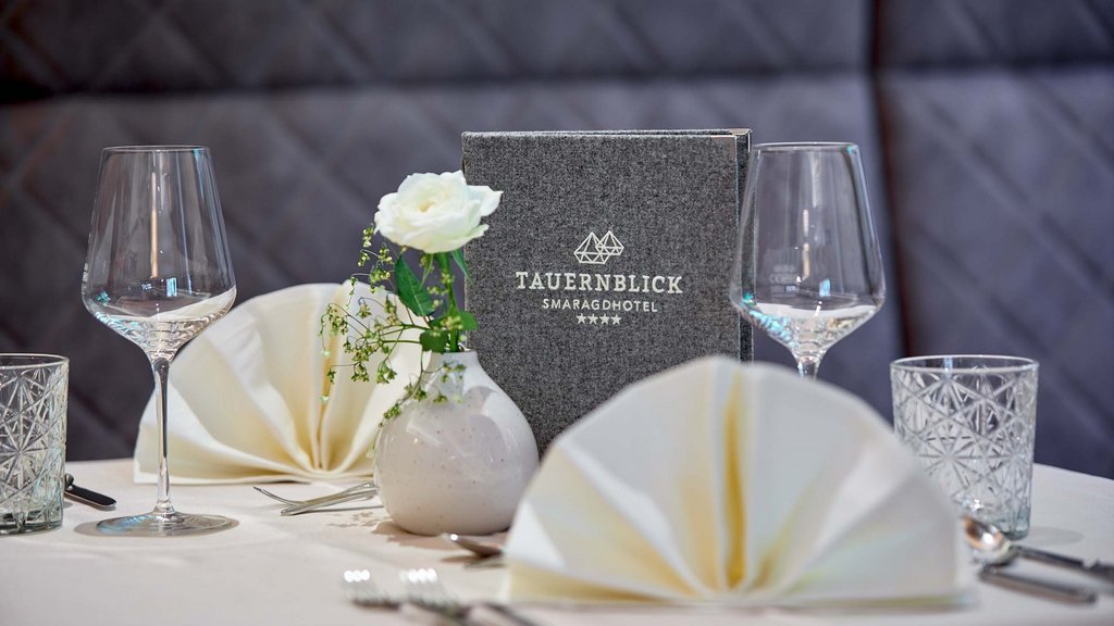 Ihr Pärchenurlaub in Österreich Gedeckter Tisch mit gefaltetem Stoffservietten, Glas und Menü im Tauernblick Smaragdhotel.