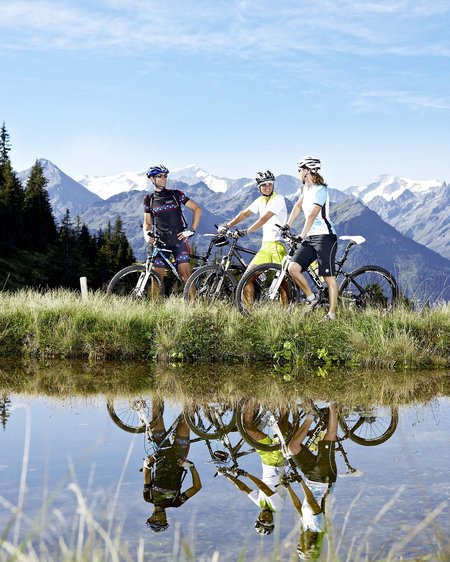 Bramberg am Wildkogel: accommodation Three mountain bikers with bikes by lake reflecting them and alpine mountain backdrop