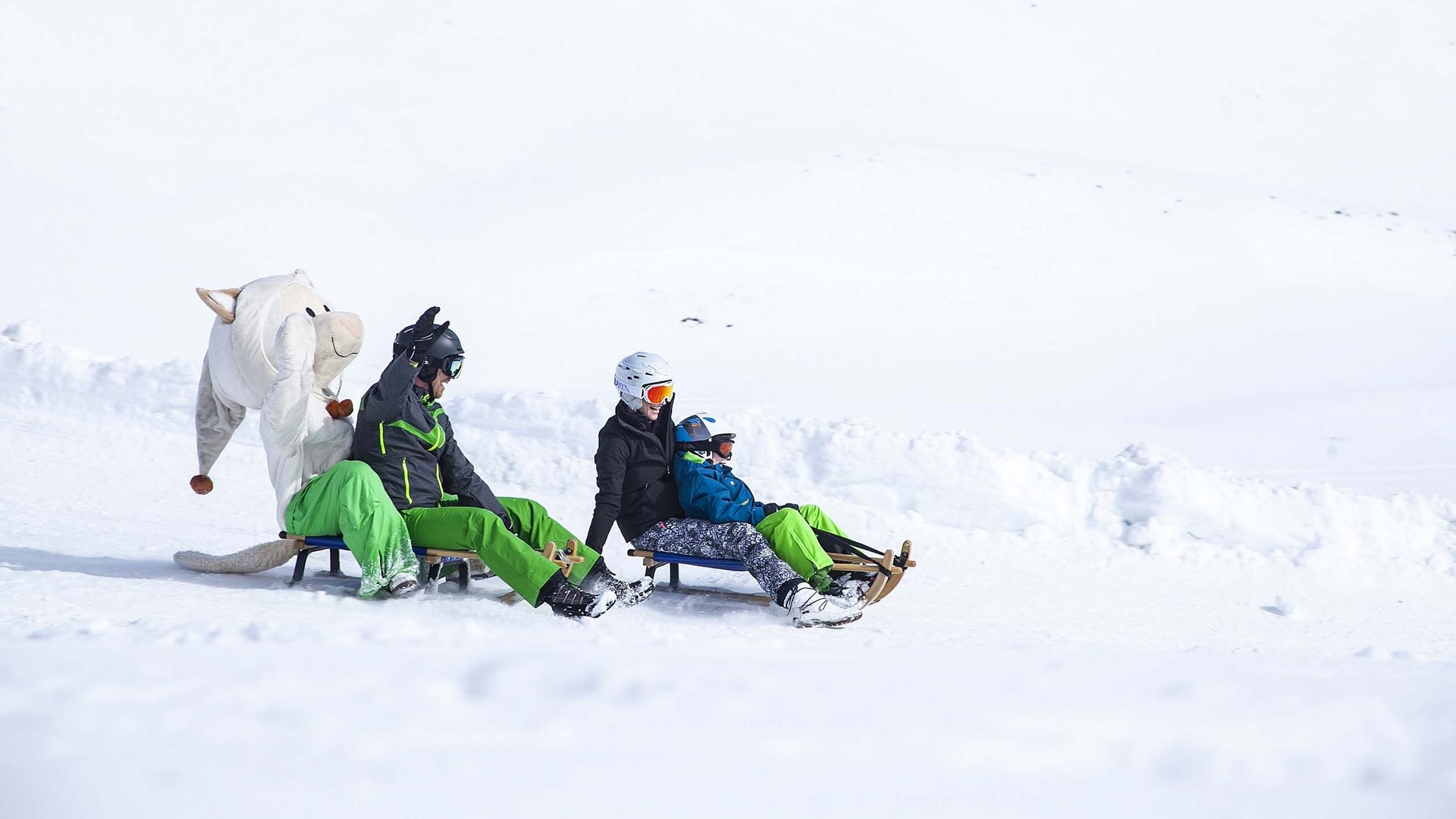 Spaß beim Rodeln: Bramberg am Wildkogel Menschen und eine Person in Tierkostüm rodeln zusammen im Schnee