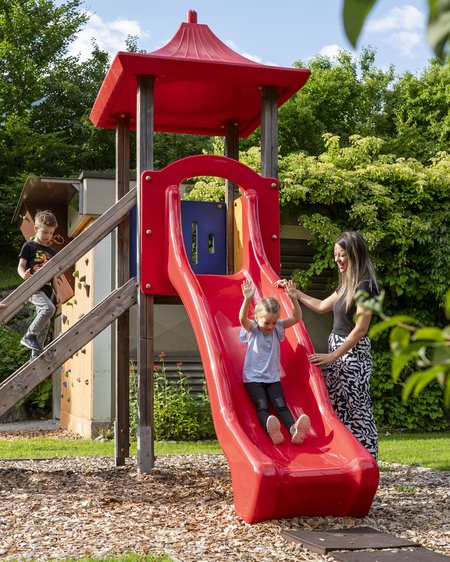 Hotel in Bramberg: Smaragdhotel Tauernblick Kinder rutschen auf roter Rutsche im Park, Eltern begleiten sie