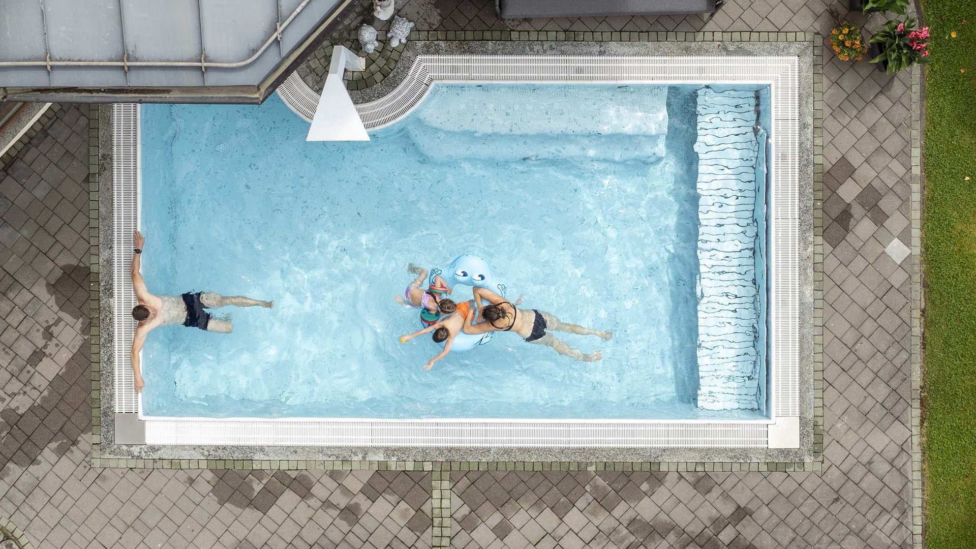 Family hotel in Austria with pool Aerial view of a rectangular pool with people and children's toy in the water
