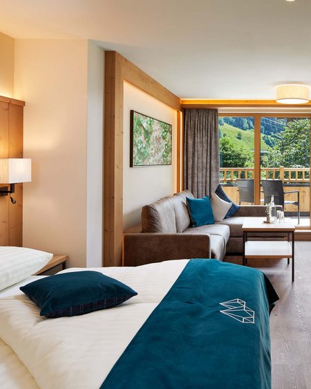 Bramberg am Wildkogel: accommodation Modern hotel room with bed, sofa, and balcony overlooking green mountains