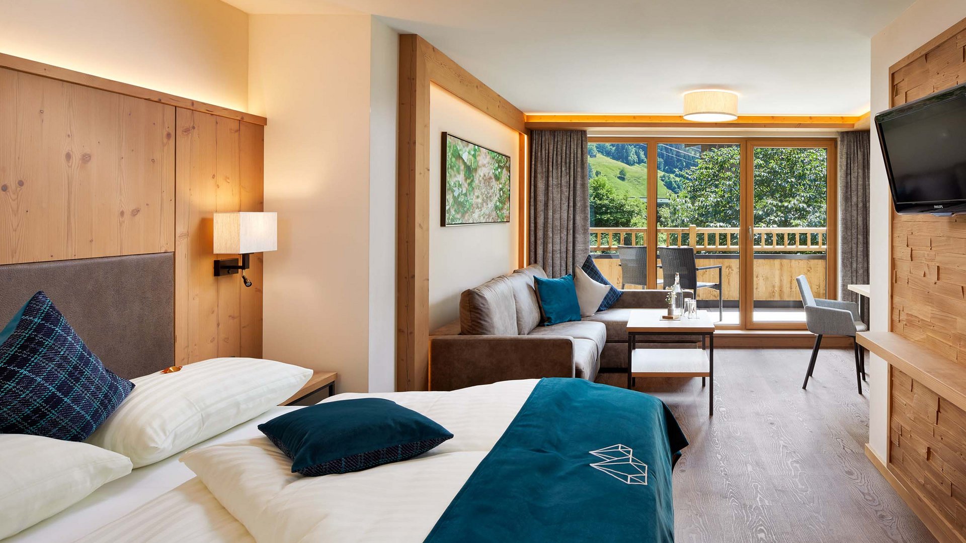 Skiurlaub mit Kindern in Österreich Modern eingerichtetes Hotelzimmer mit Bett, Sofa und Balkon mit Bergblick