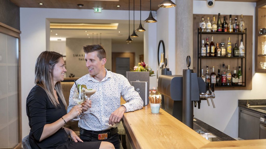 Smaragdhotel Tauernblick – Ihr 4-Sterne-Hotel am Wildkogel Paar unterhält sich und trinkt Cocktails an einer Hotelbar mit Holztheke