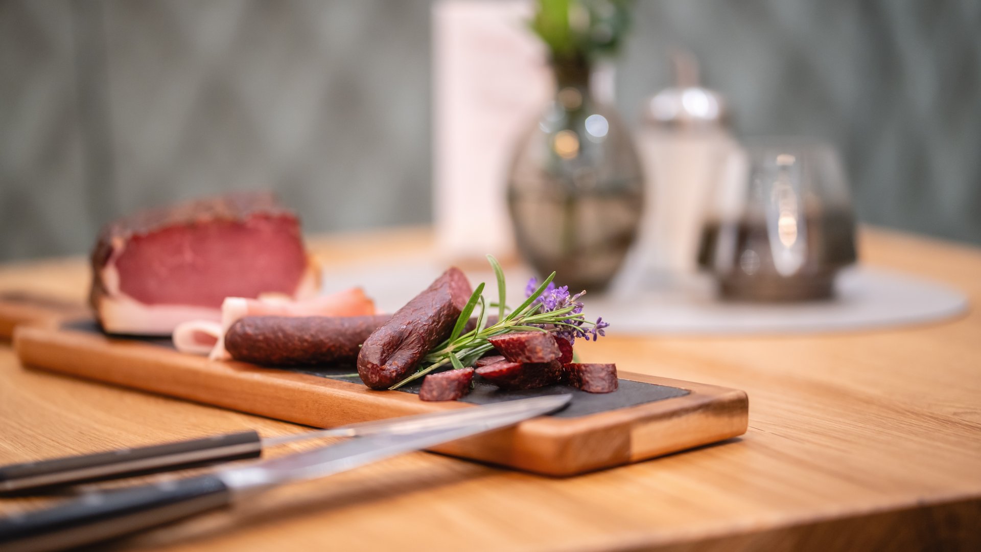 Wellnesshotel Salzburgerland: Smaragdhotel Tauernblick Aufgeschnittene Wurst und Schinken auf einem Holzbrett mit Kräutern