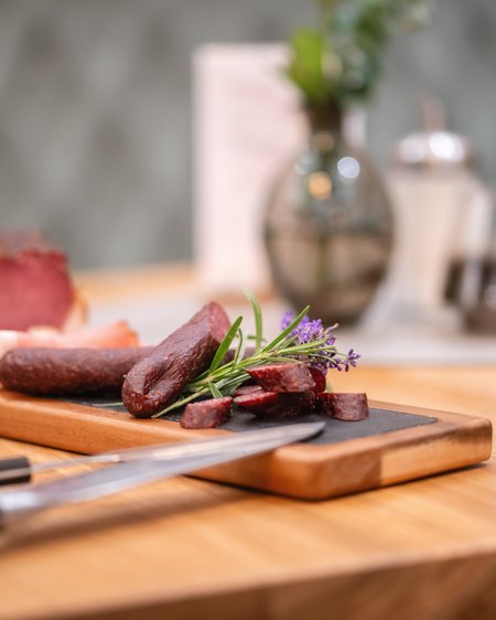 Family hotel in Salzburgerland: 4-star inclusive services Sliced sausage and ham on a wooden board with herbs