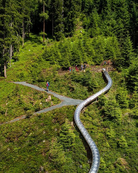 Hotel in Bramberg: Smaragdhotel Tauernblick Long slide in forest with hikers on path surrounded by green trees