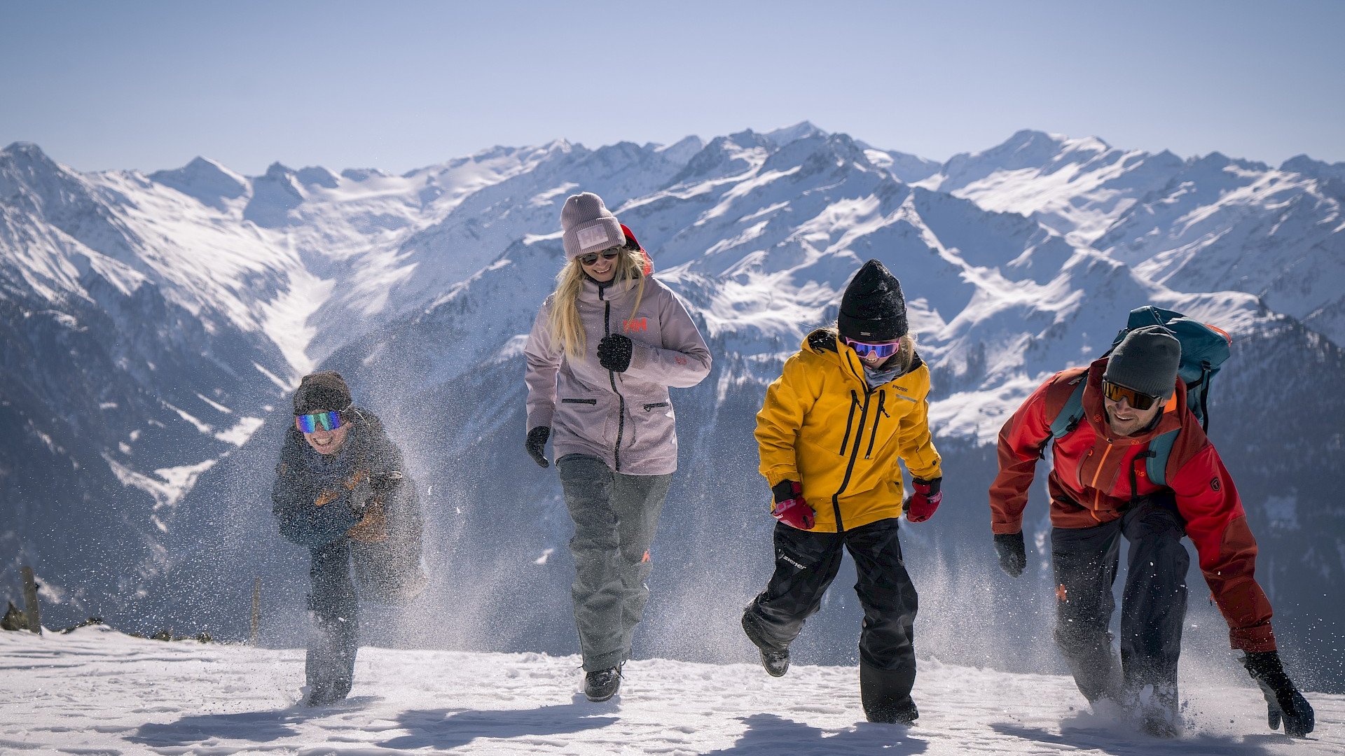 Family hotel in Bramberg: Smaragdhotel Tauernblick Four people walking in snow with snowy mountains in the background on a sunny day