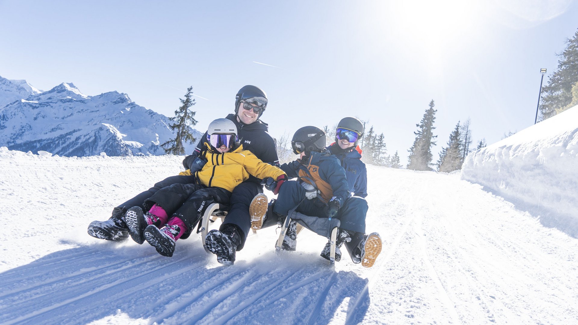 Family hotel in Bramberg: Smaragdhotel Tauernblick Family sledding together down a snowy slope on a sunny day
