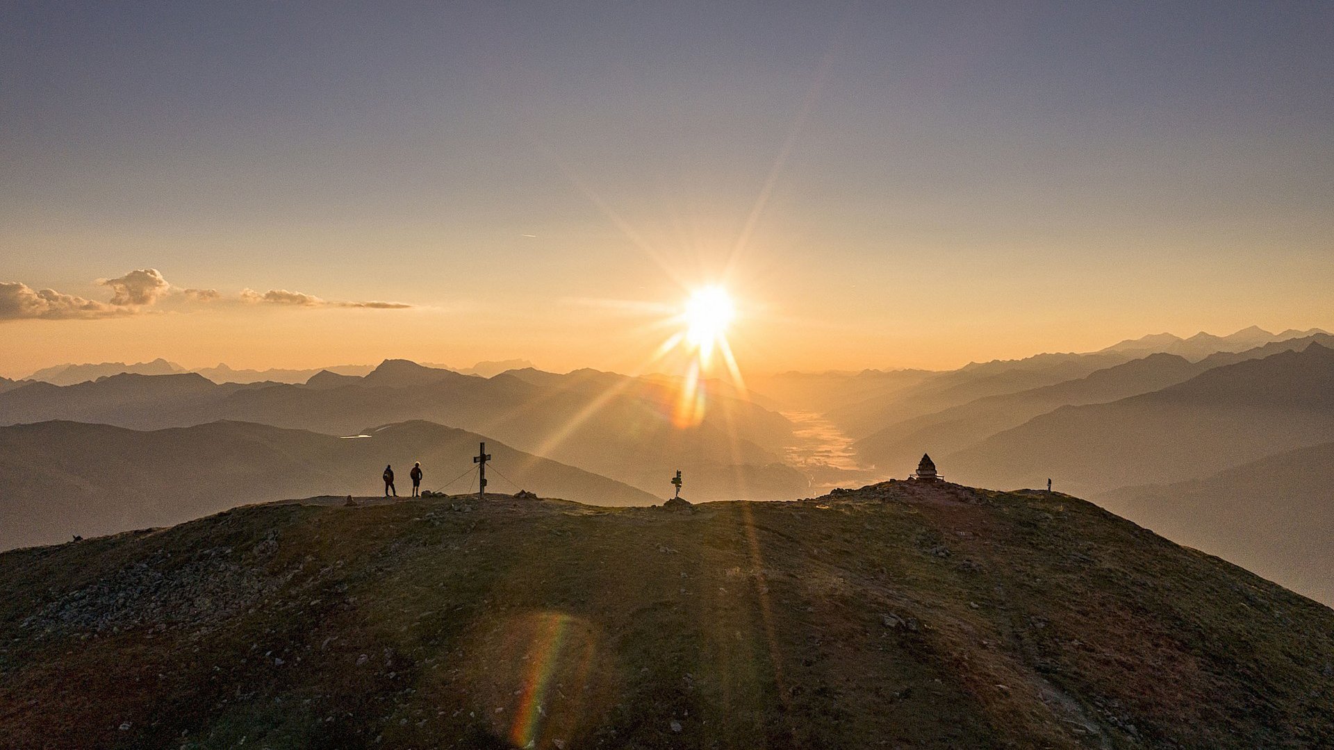 Familienhotel: Österreich im Sommer erleben Sonnenuntergang über bergigem Panorama mit zwei Wanderern auf dem Gipfel