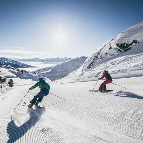 Die besten Hotels im Salzburgerland Zwei Skifahrer fahren bei sonnigem Wetter auf einer präparierten Skipiste