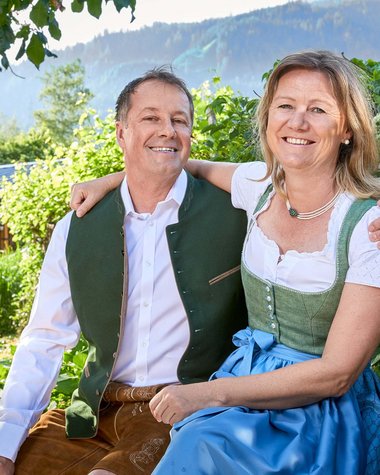 Wildkogel: Hotel mit Blick für das Besondere Paar in traditioneller bayerischer Tracht in einem Garten vor Bergkulisse