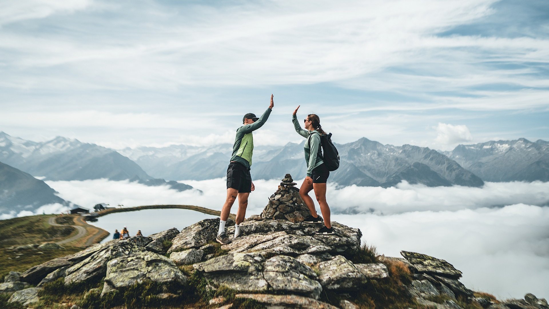 Bramberg am Wildkogel: Ausflugsziele Zwei Wanderer geben sich auf einem Berggipfel vor Nebeln und Bergen ein High Five