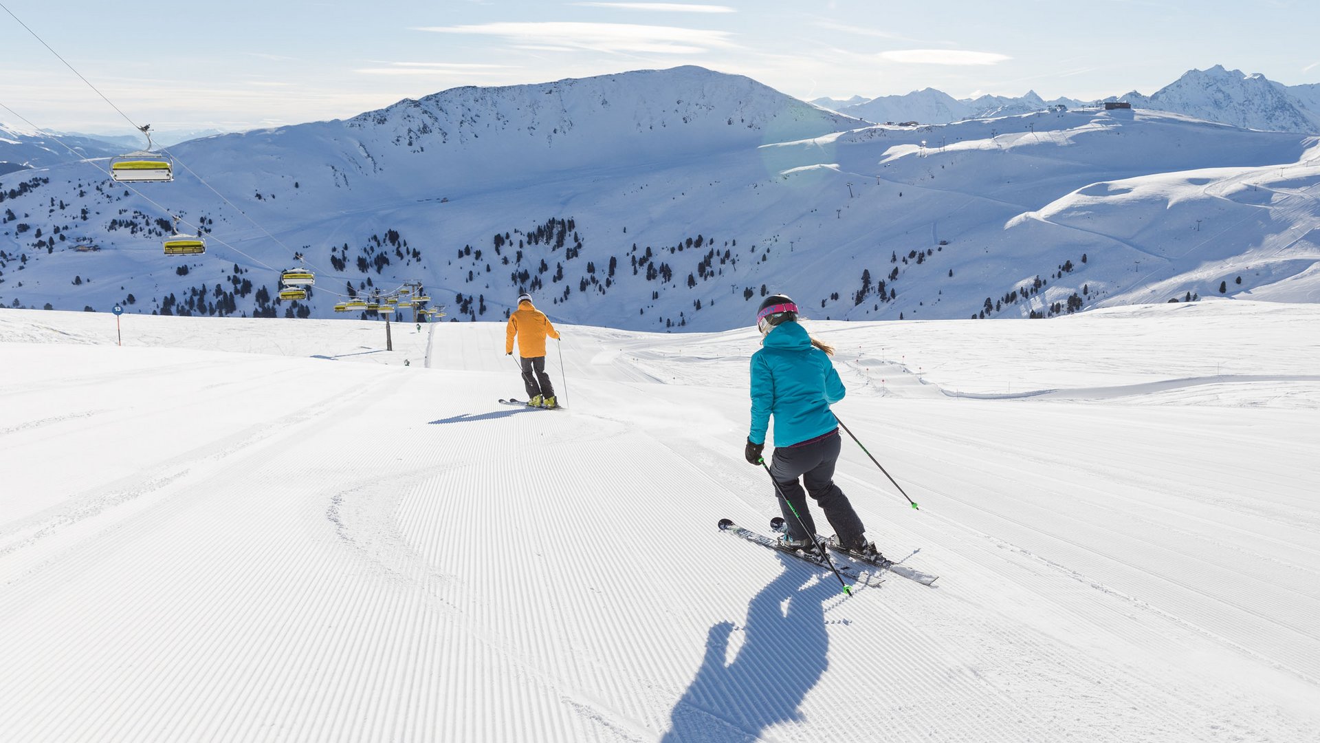 Skiing holidays in Salzburgerland: Smaragdhotel Tauernblick Two skiers on freshly groomed slope with snowy mountains in the background