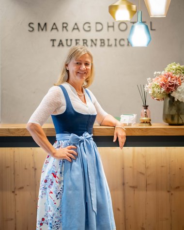 Wildkogel: Hotel mit Blick für das Besondere Frau im Dirndl steht lächelnd an der Rezeption des Smaragdhotels Tauernblick